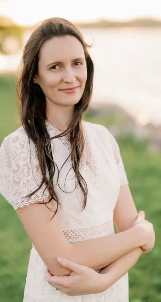 Smiling woman in a white lace top with her arms folded, outdoors